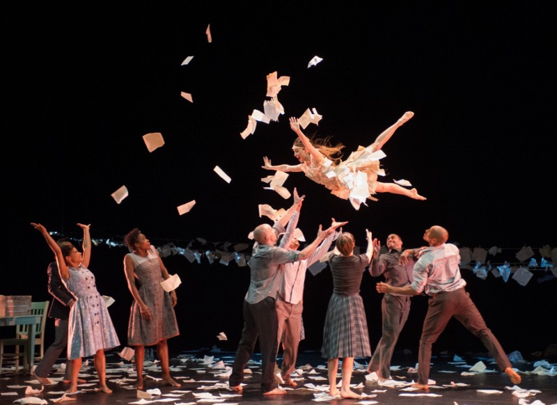 dancer flying through the air as paper sheets fly and hang in the background on a close line